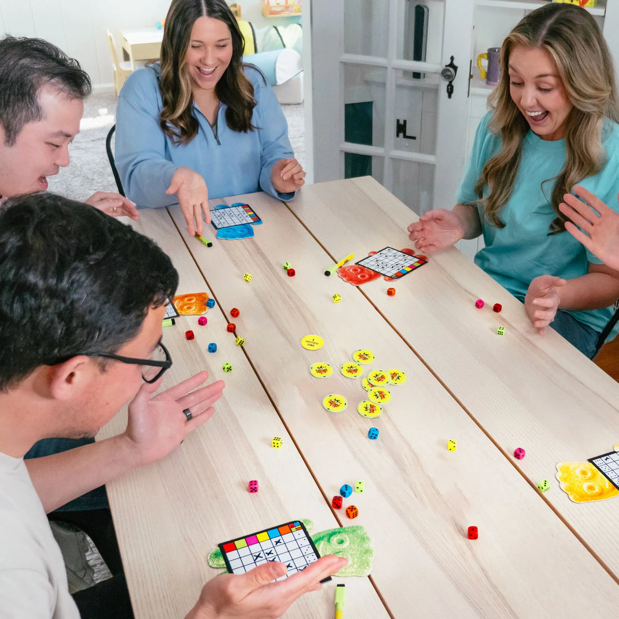 Four people playing Sixem Sour Patch Kids dice game at a wooden table, smiling and having fun.