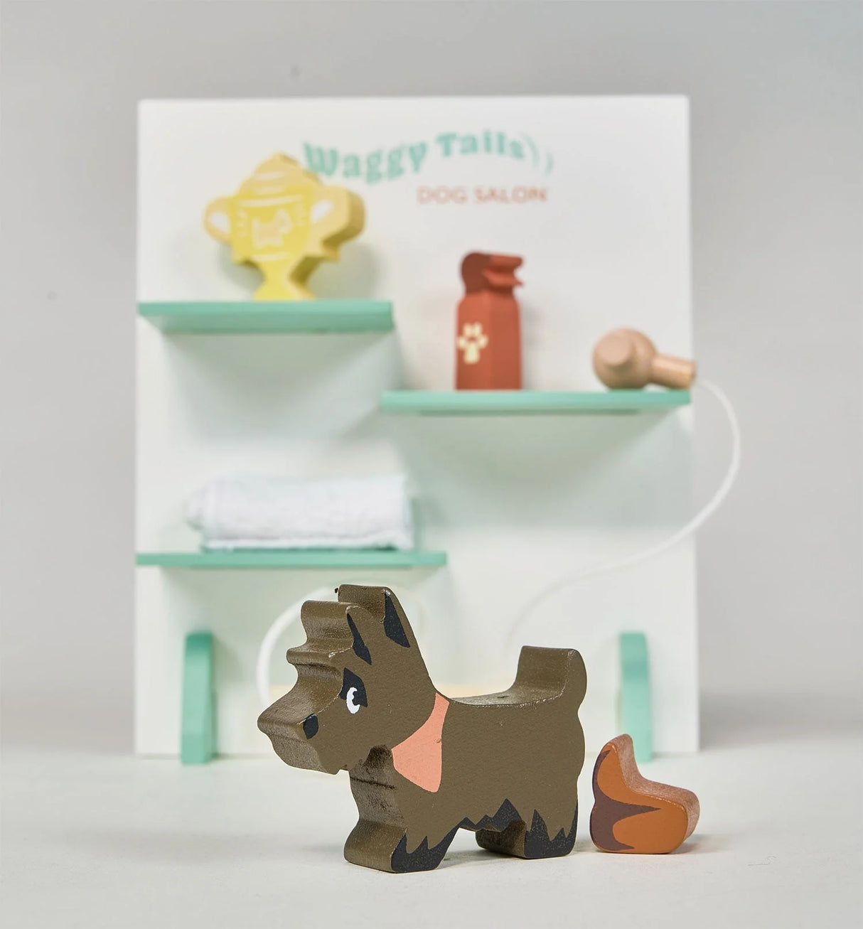 Waggy Tails Dog Salon play set featuring a wooden Scotty dog, grooming tools, and a towel on shelves.
