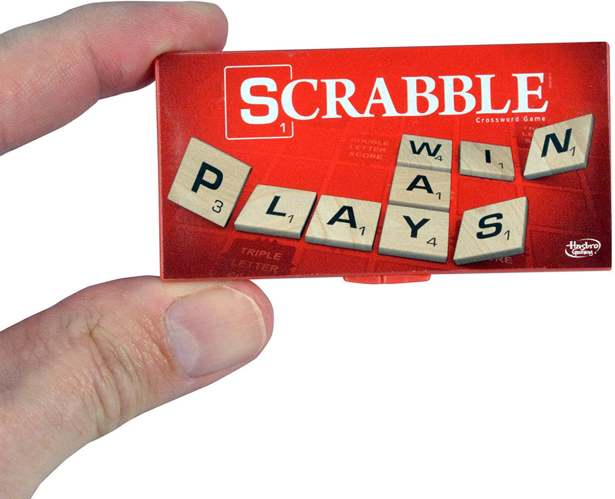 Hand holding the world's smallest Scrabble game box with letter tiles spelling "PLAYS WIN" on the cover