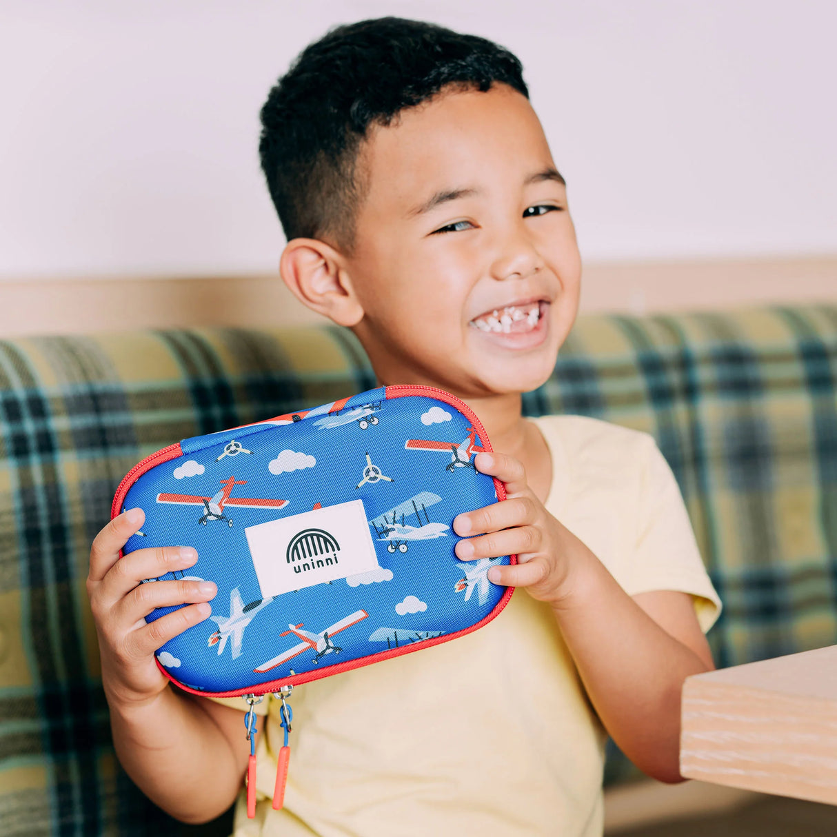 Child holding a blue Pencil Case | Airplane with red trim featuring airplane designs and a uninni logo.