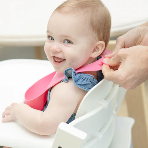 Baby wearing a pink Wonder Bib | It's Me Hi silicone bib with adjustable neck closure being fastened.