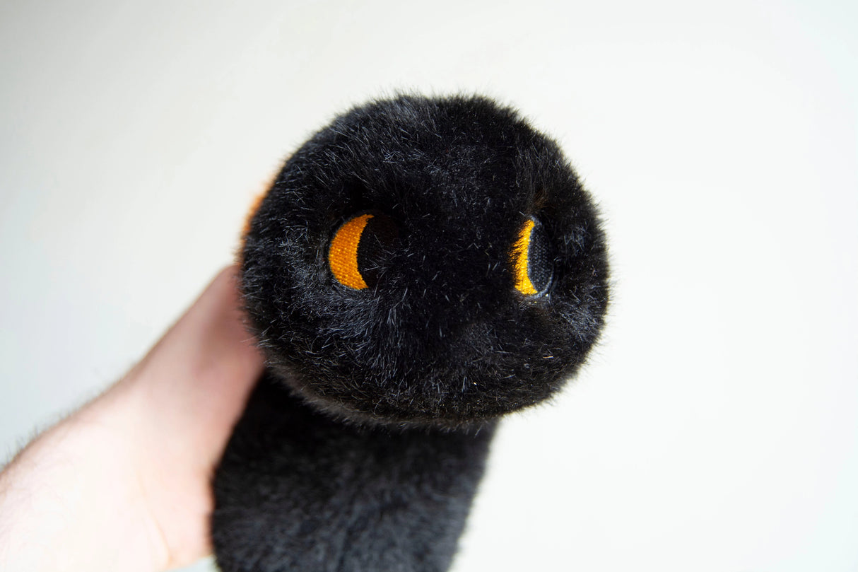 Close-up of a black Wooly Bear Caterpillar weighted plush with soft faux fur and embroidered yellow eyes held in hand