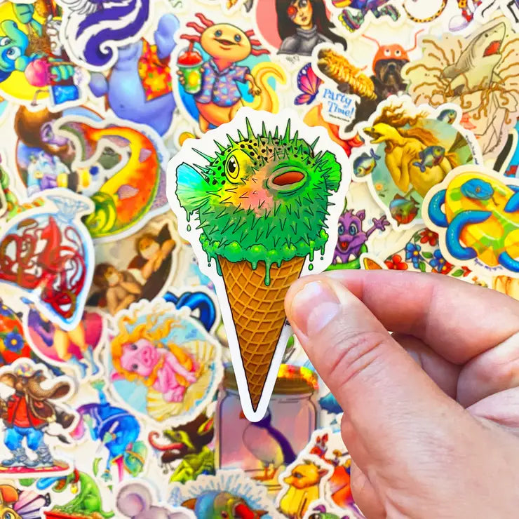 Hand holding a Pufferfish Ice Cream Cone Sticker with a colorful background of various vinyl stickers.