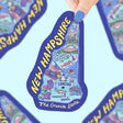 Hand holding a colorful New Hampshire map sticker featuring landmarks and cities on durable vinyl material