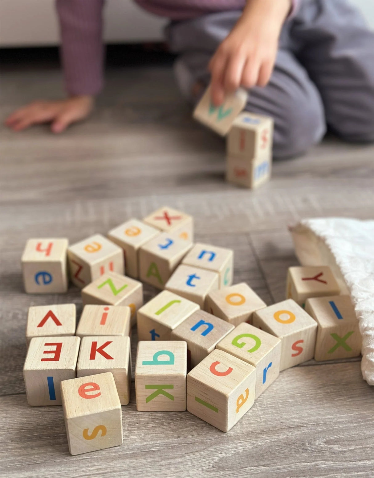 Child playing with colorful wooden alphabet blocks spilled from a white drawstring bag on the floor