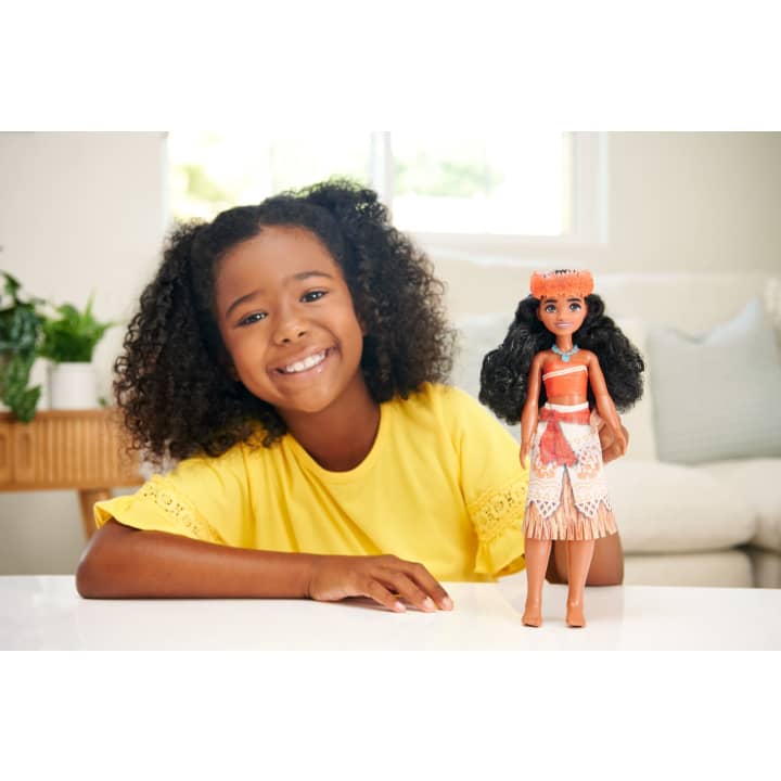 Disney Princess Moana doll with removable necklace and headband, long wavy hair, and signature outfit next to smiling child.