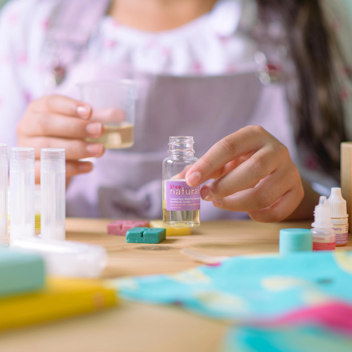 Person making lip balm using organic ingredients in a DIY Lip Balm Kit with bottles and accessories on a table.