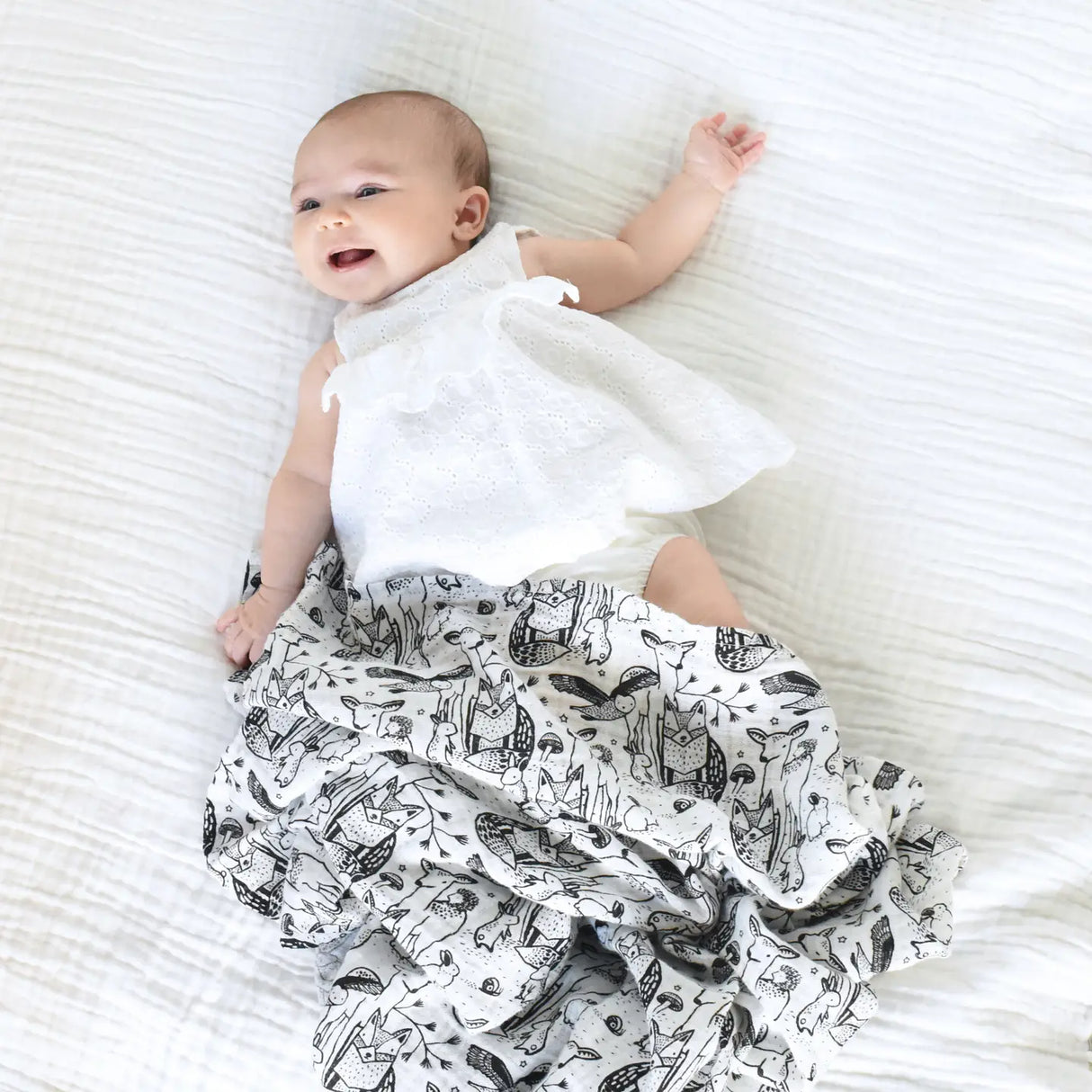 Organic Muslin Swaddle | Forest with black and white animal print wrapped around a smiling baby lying on a white blanket