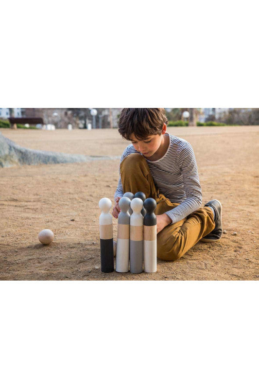 Child setting up beech wood pins and balls for Bowling game on outdoor dirt surface, enjoying classic fun.