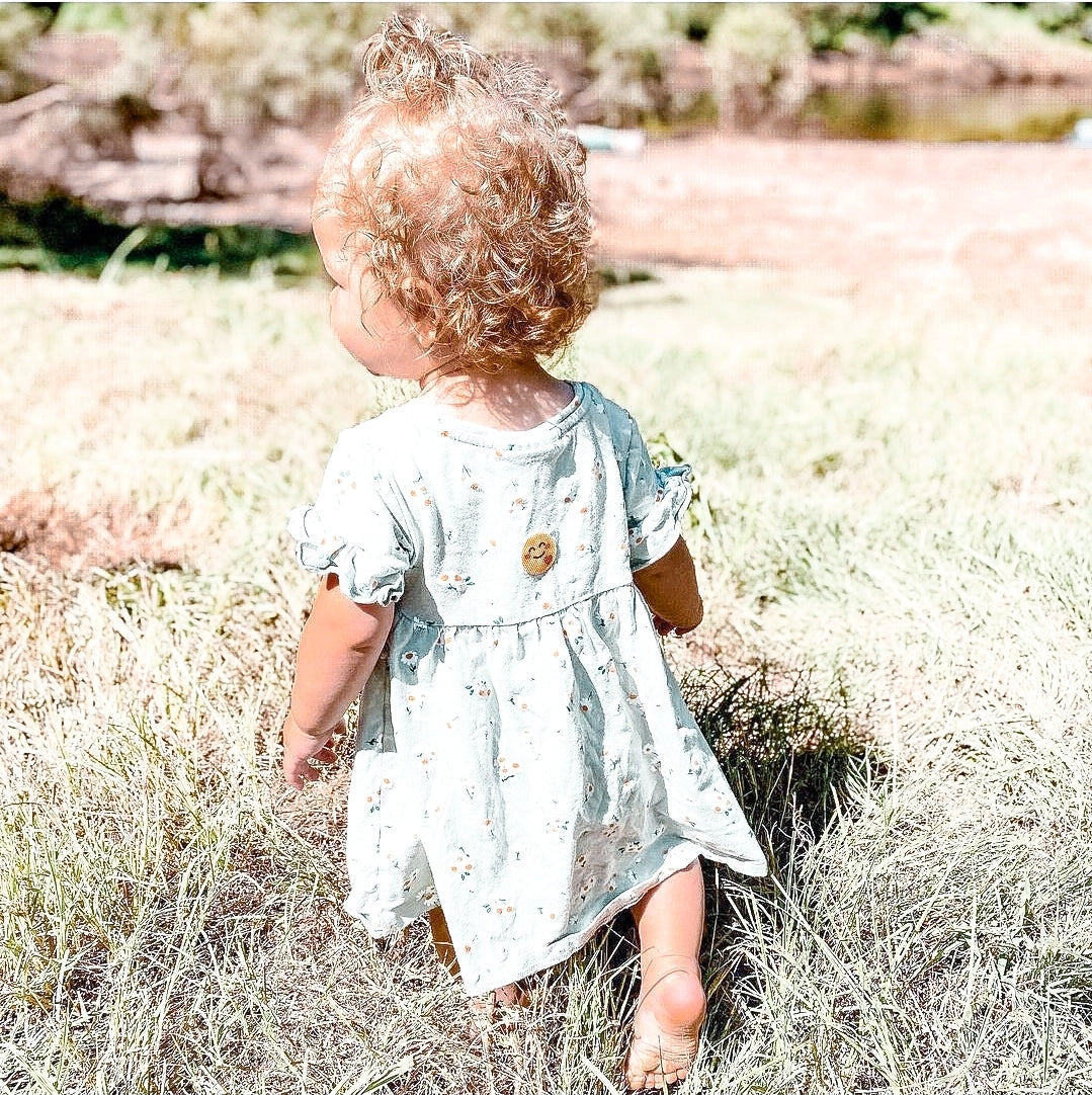 Toddler wearing Natpat | Buzzpatch Mosquito & Insect Repellent Stickers on dress outdoors in grassy area.