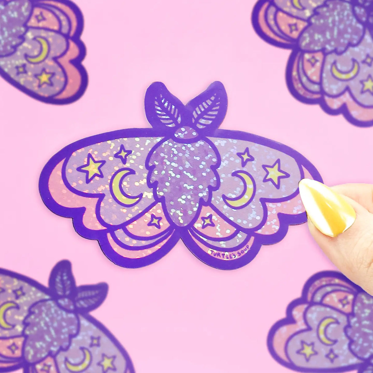 Moon Moth Glitter Sticker showing a purple glittery moth with stars and moons on a pink background.