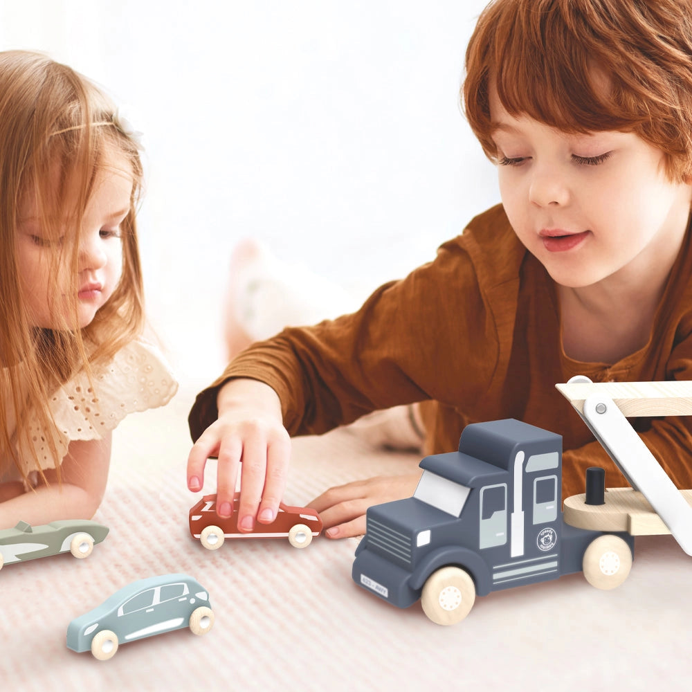 Two children playing with a wooden car transporter truck toy and four colorful wooden cars on a light surface