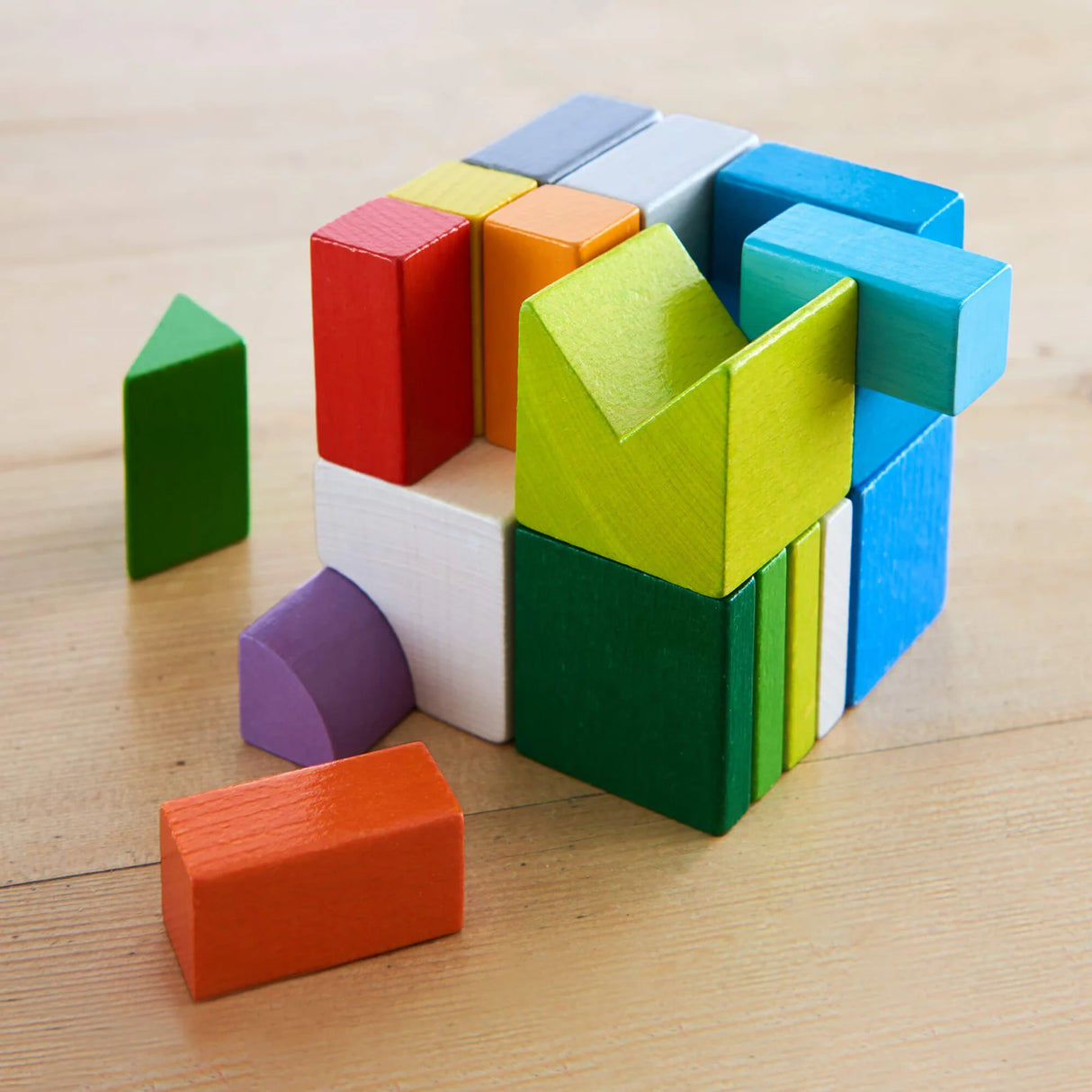 Colorful wooden blocks arranged in a 3D puzzle forming a cube on a wooden surface with some pieces outside