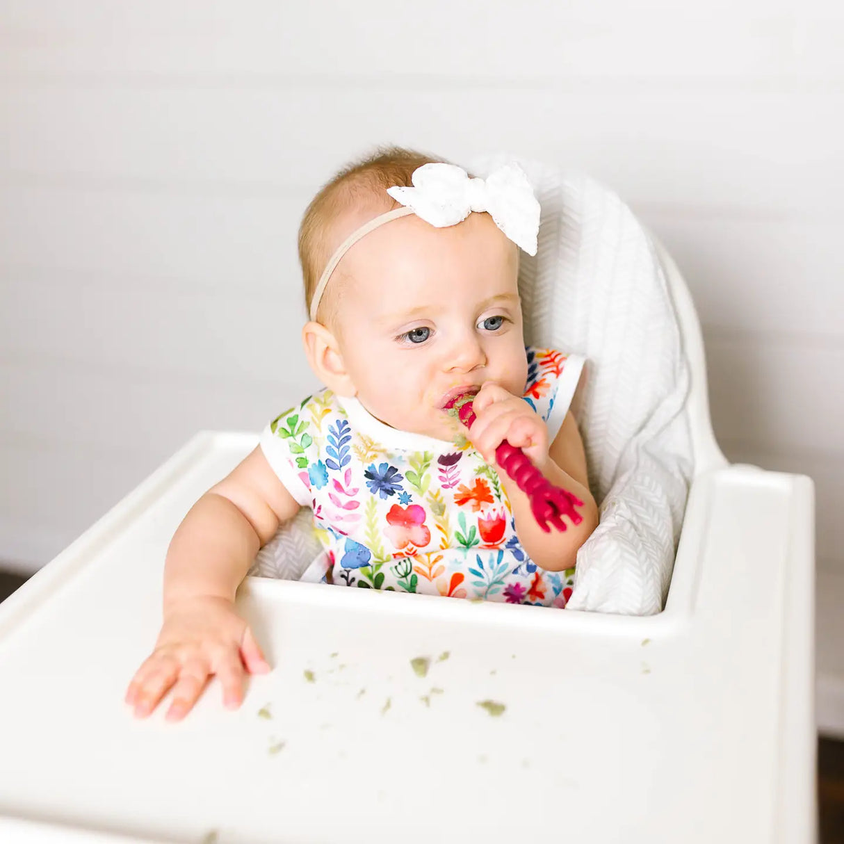 Baby wearing Bapron | Rainbow Watercolor 6M-3T sitting in high chair during mealtime with food on tray.
