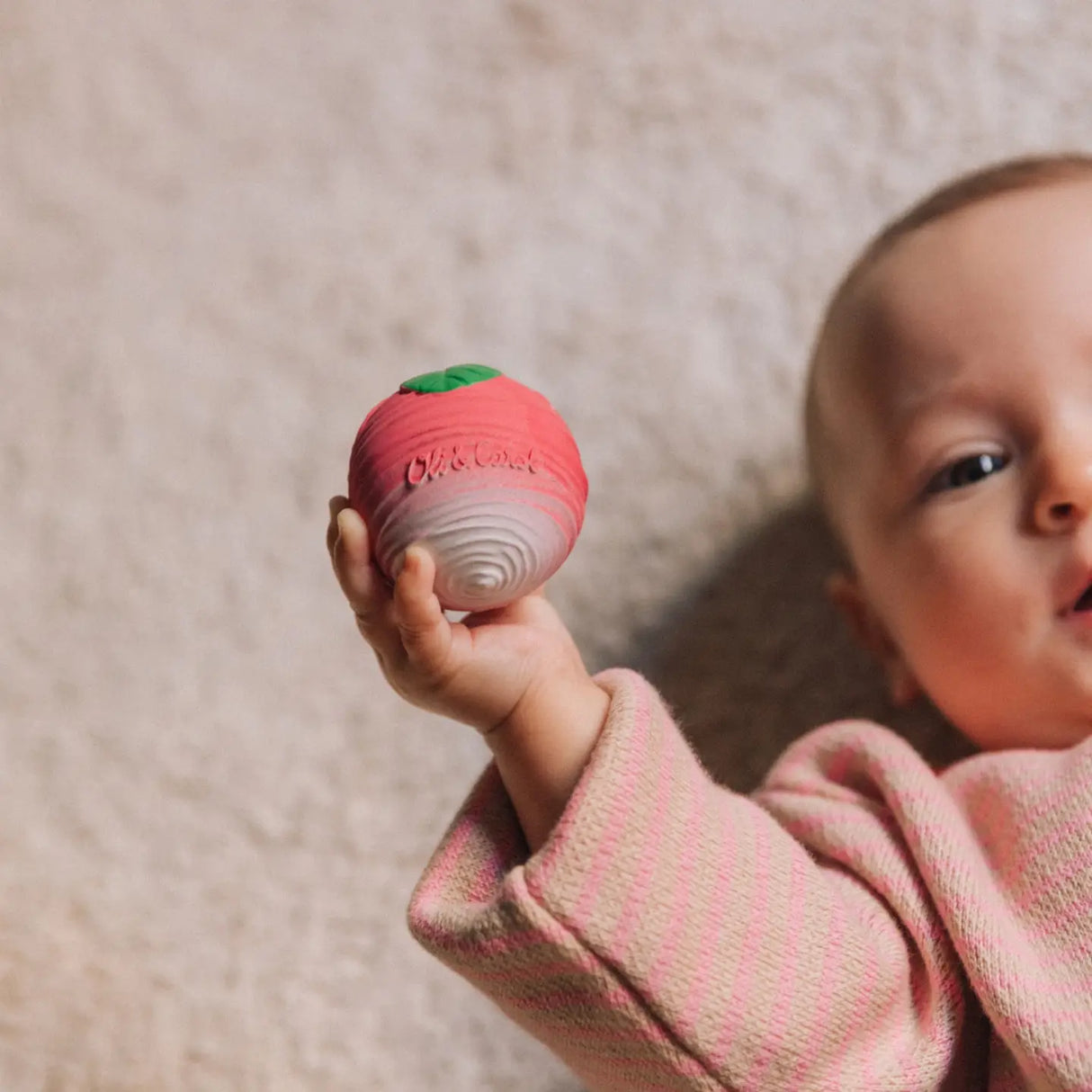 Baby holding a textured radish-shaped sensory ball made of soft natural rubber for teething and play