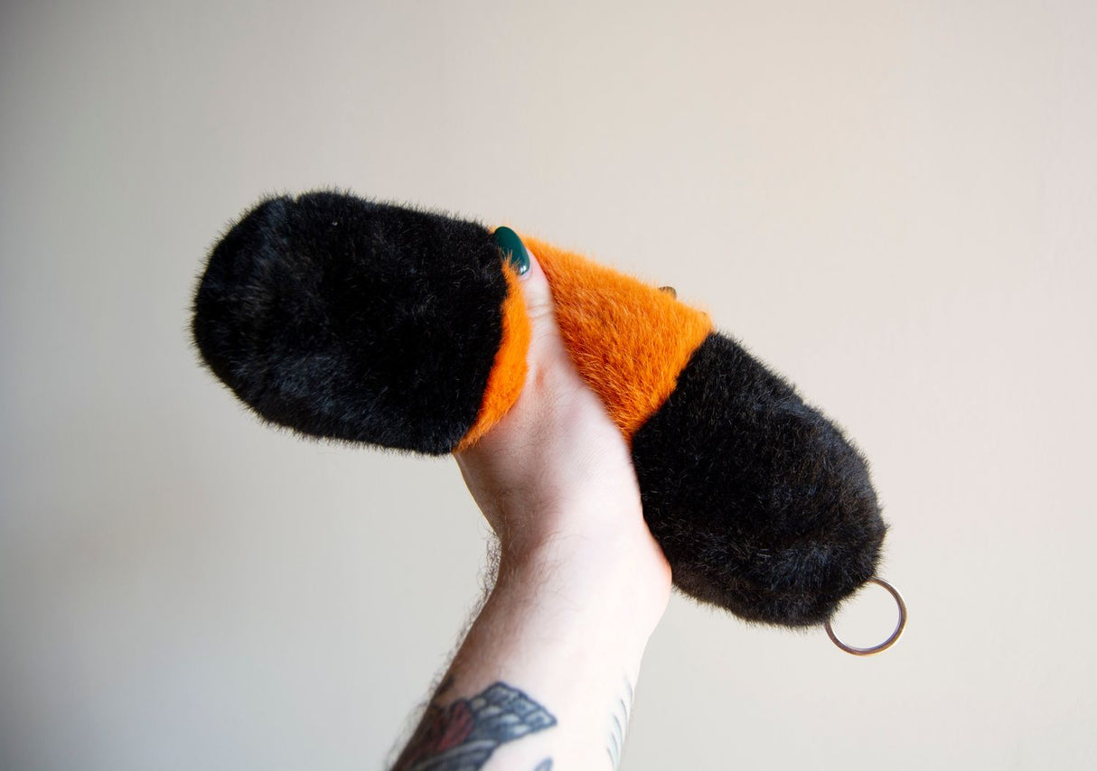 Hand holding a large weighted plush Wooly Bear caterpillar keychain with soft black and orange faux fur