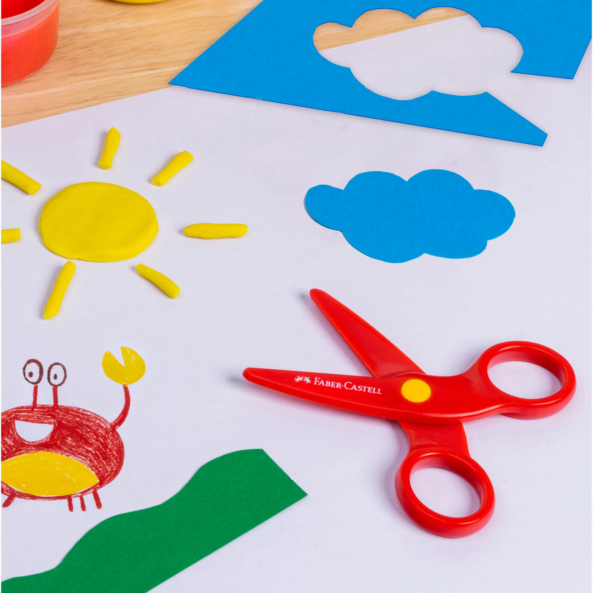 Little Creatives Play Safe Scissors in red with kid-safe blades next to colorful paper crafts and modeling dough.