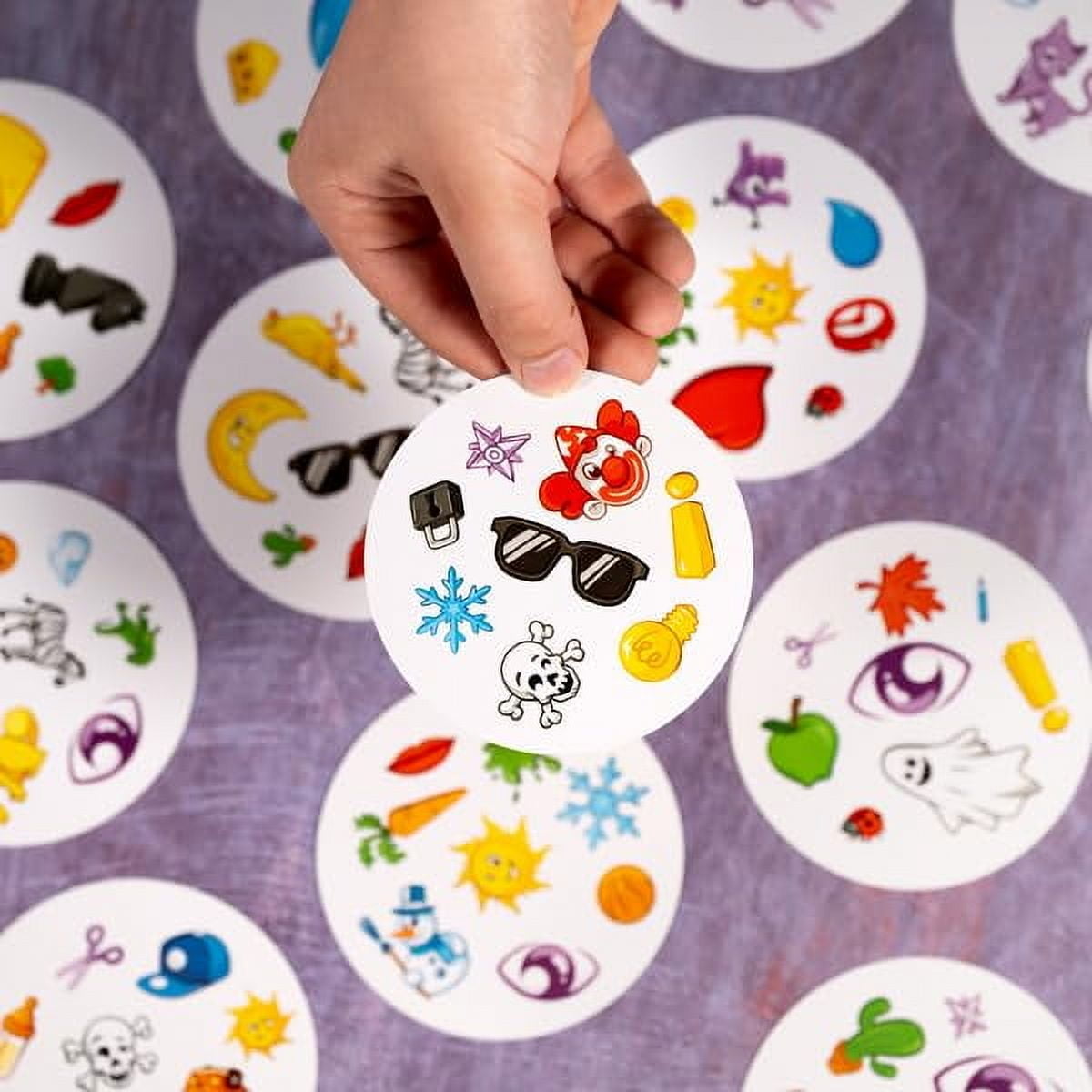 Hand holding a Spot It! card showing colorful icons in a fast-paced matching game for all ages.