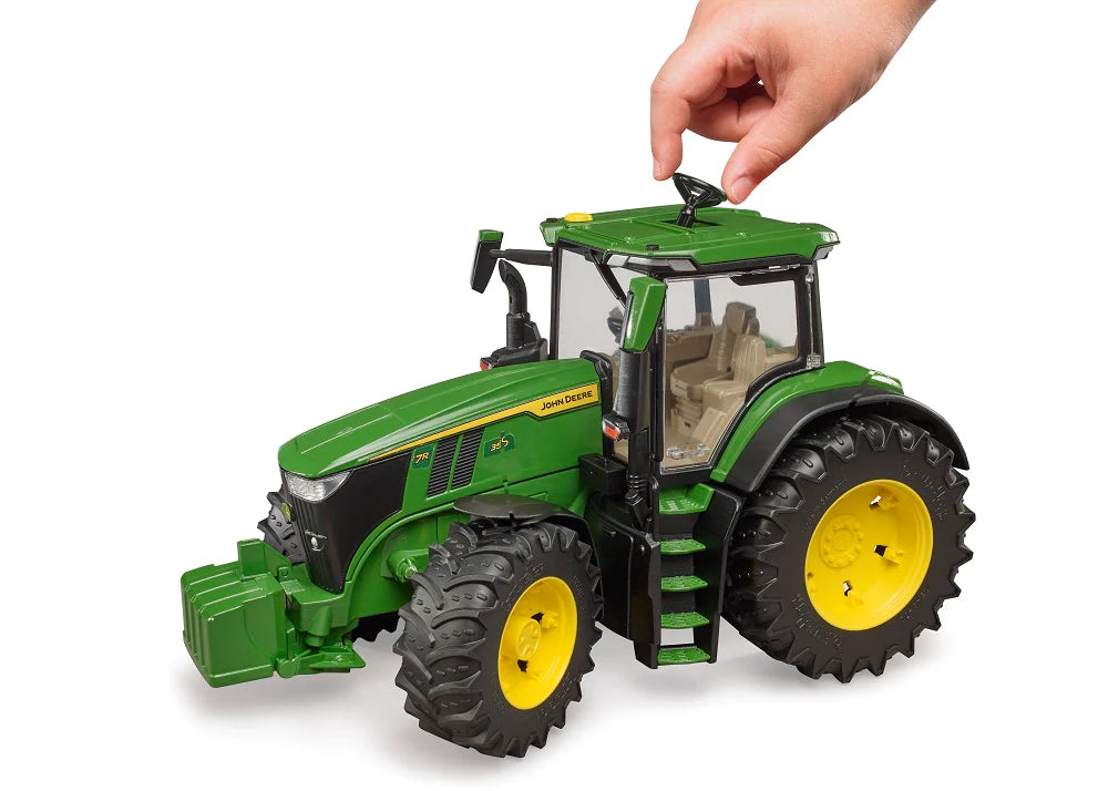 Child's hand adjusting steering wheel on John Deere 7R 350 Tractor toy with glazed cabin and large tires.