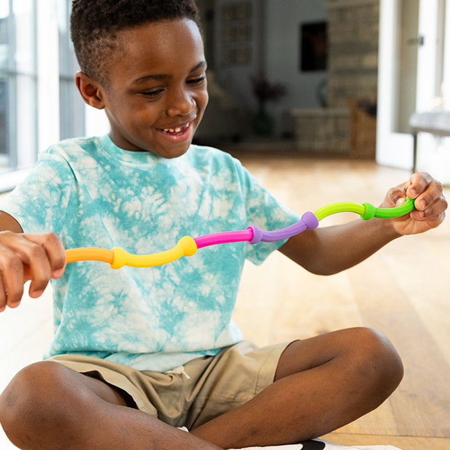 Child playing with colorful linked pieces using Plip Links for creative sensory play and fine motor skills development.