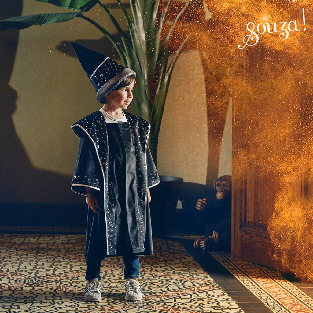 Child wearing deep blue wizard coat with silver stars and matching pointed hat casting a magical spell indoors