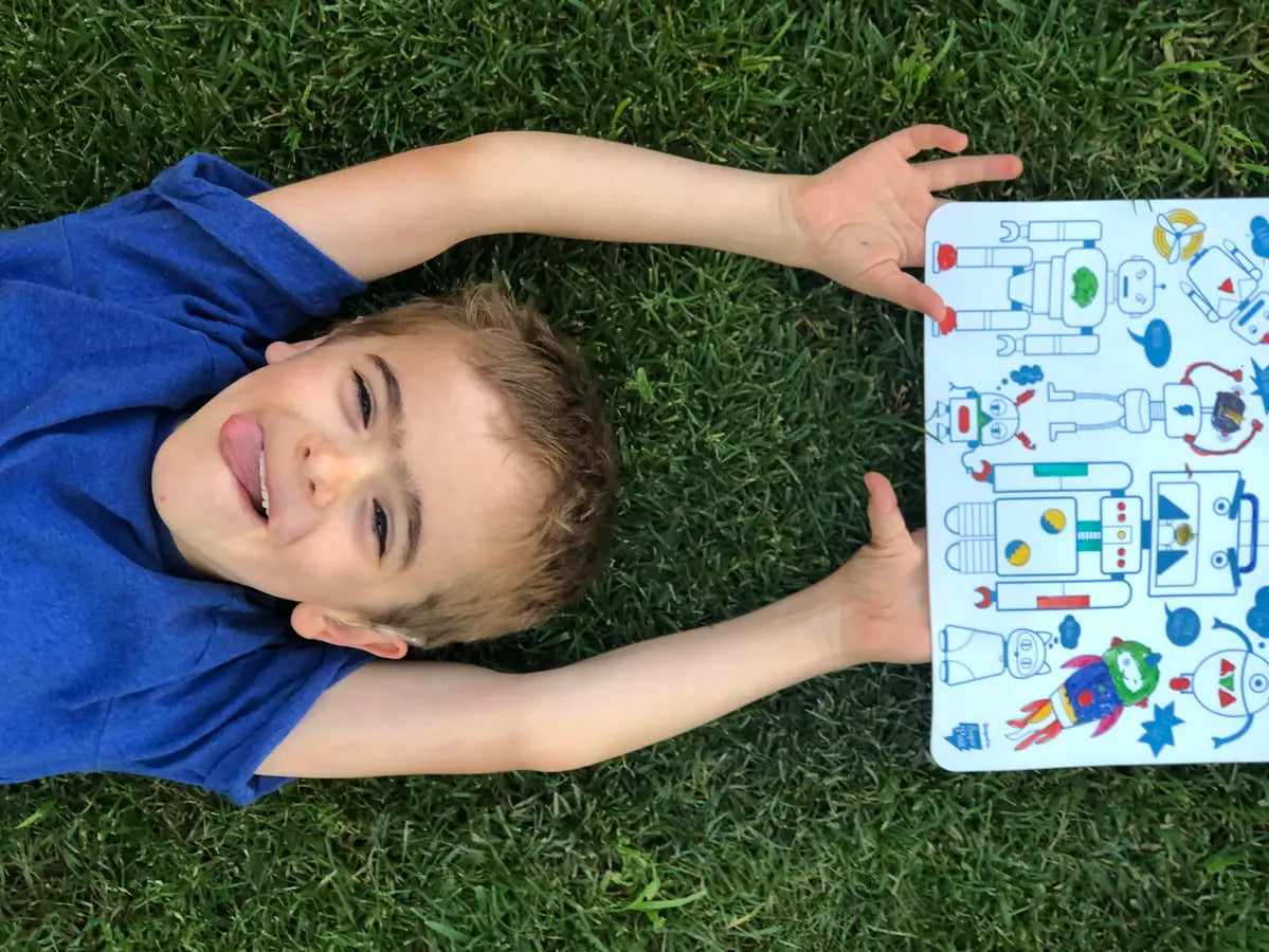 Child lying on grass holding Mini Play Mat Robot with colorful reversible robot silicone drawing mat and markers