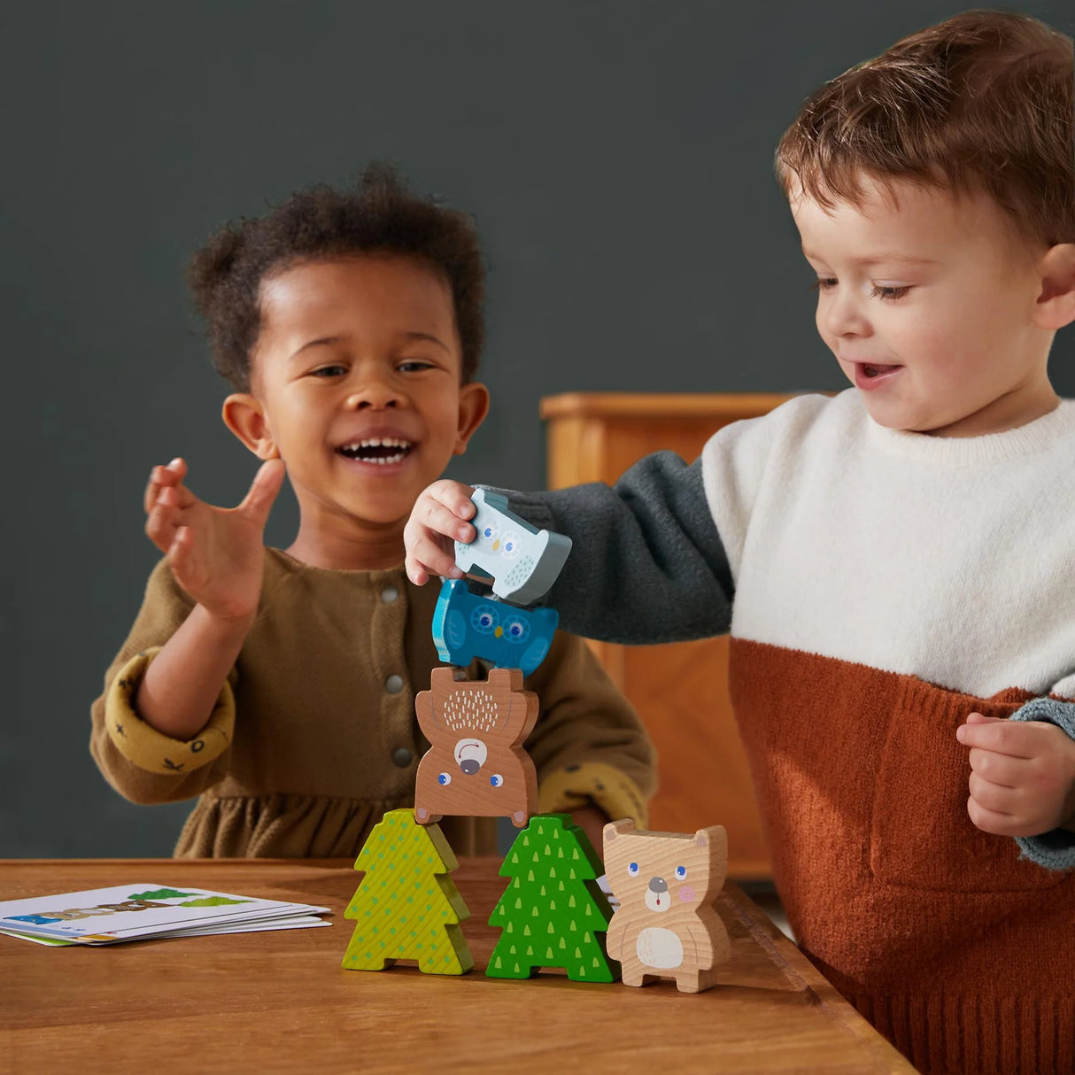 Two children happily stacking animal and tree blocks with the Forest Friends Stacking Toy on a wooden table