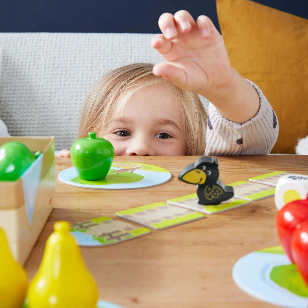 Child reaching to move wooden pieces in a colorful cooperative fruit orchard board game on a wooden table