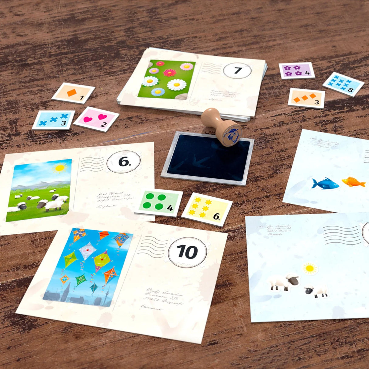 Postcards with different images and numbered stamps laid out on a wooden surface for a math postage game