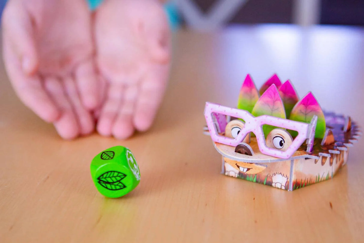 Child playing Hedgehog Haberdash game with colorful hedgehog figure, green leaf dice on wooden table background