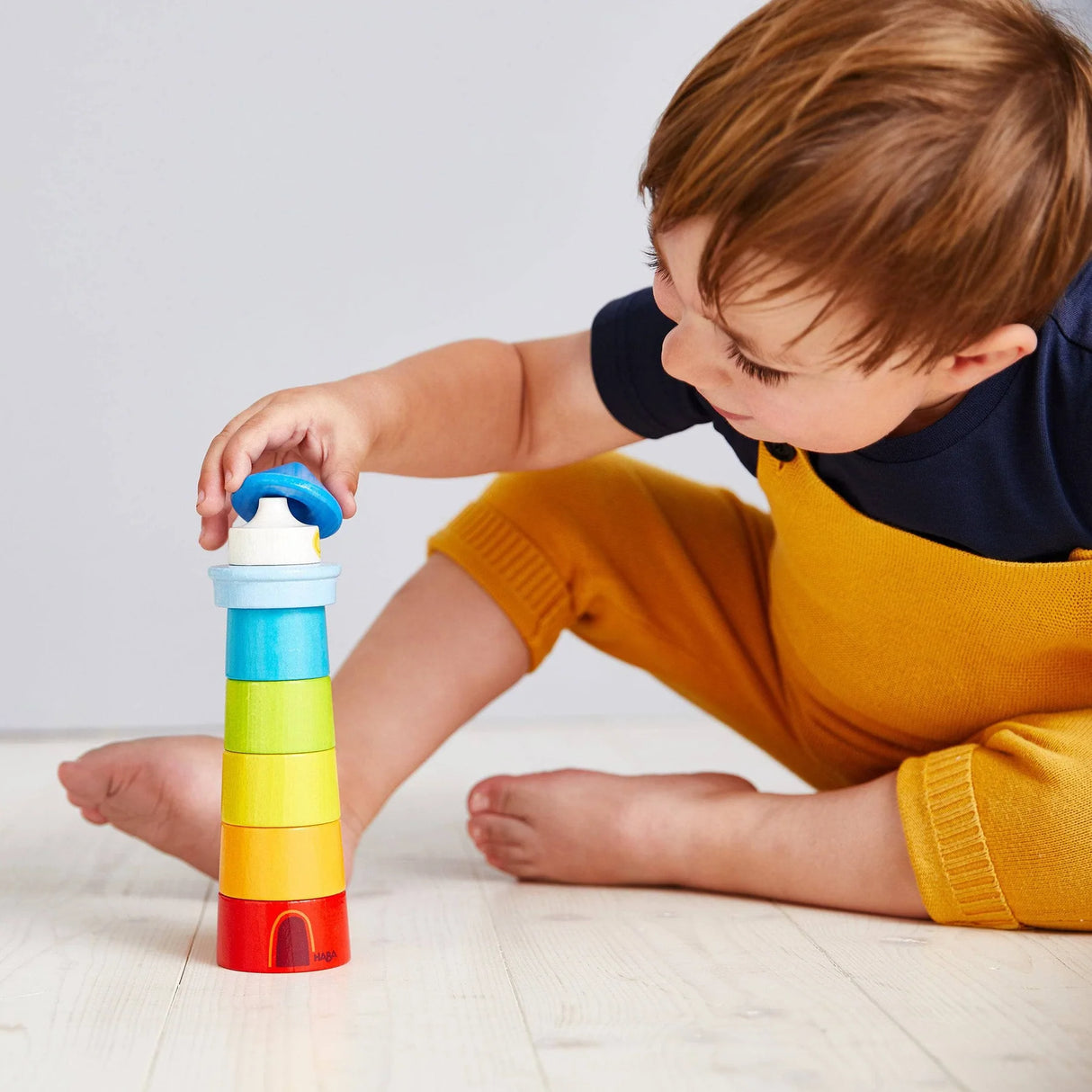 Young child playing with colorful stacking lighthouse toy on light wooden floor indoors