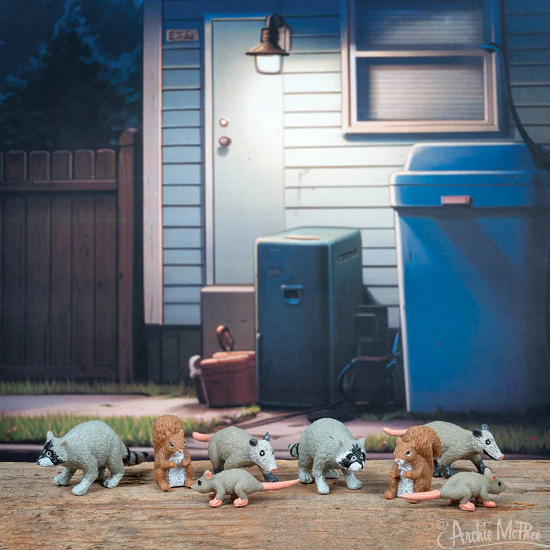 Seven small vinyl animal figurines posed in front of a city backyard scene with fence and blue siding house wall