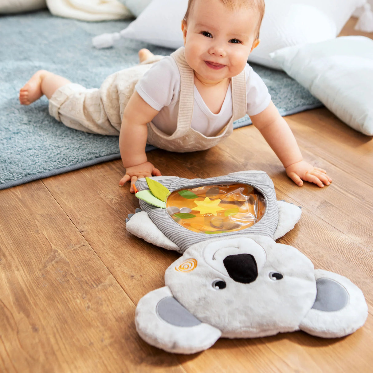 Baby playing on wooden floor with Koala Water Play Mat featuring soft fabric and floating shapes for tummy time.