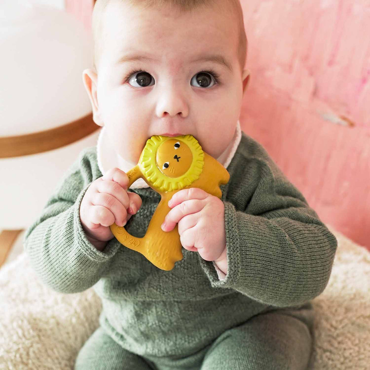 Baby holding and chewing on a yellow Richie Lion Teether made from 100% natural rubber with textured surfaces.