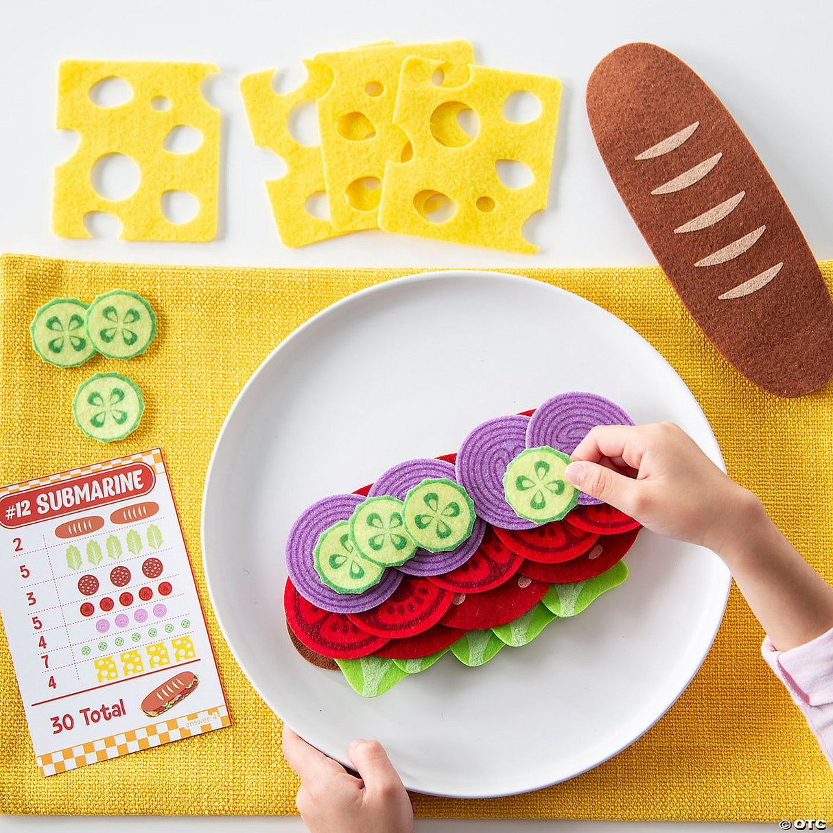 Child assembling felt sandwich with cucumber and cheese pieces using Math Sandwich educational game pieces on white plate.