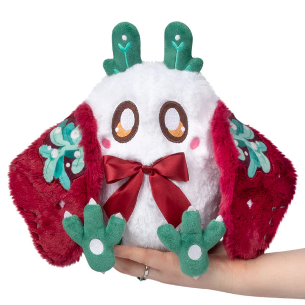 Plush white figure with large expressive eyes, red patterned wings, green leafy antlers, and a red bow on chest