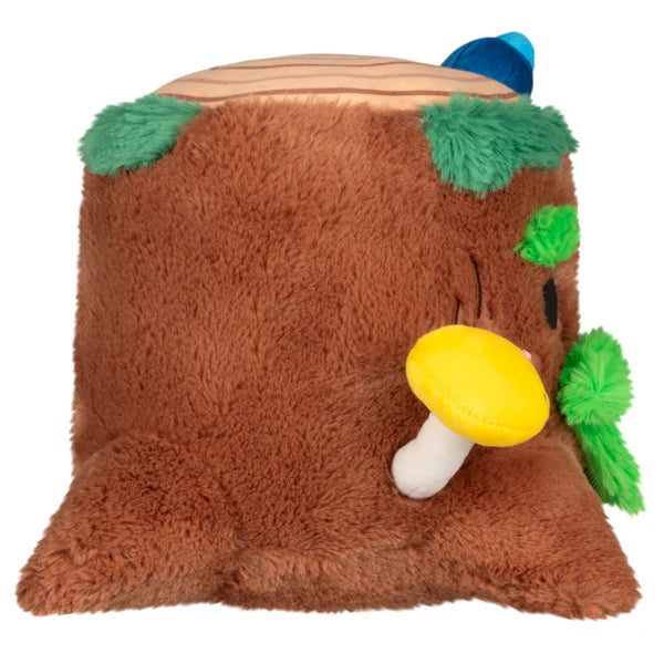 Side view of a plush tree stump. A little yellow mushroom grows out of his side, and a little blue bug perches on the top of the stump.