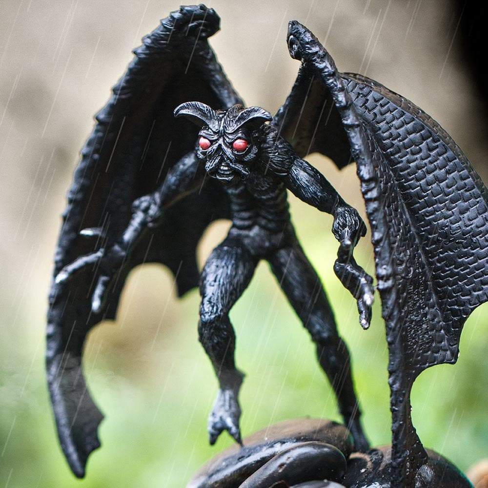 Mothman figurine with large black wings, glowing red eyes, furry body, and feathery antennae standing in rain.