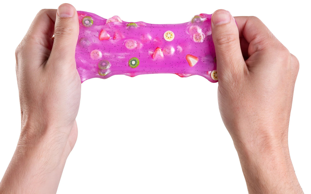 Hands pulling translucent pink slime with embedded miniature fruit slices on a white background