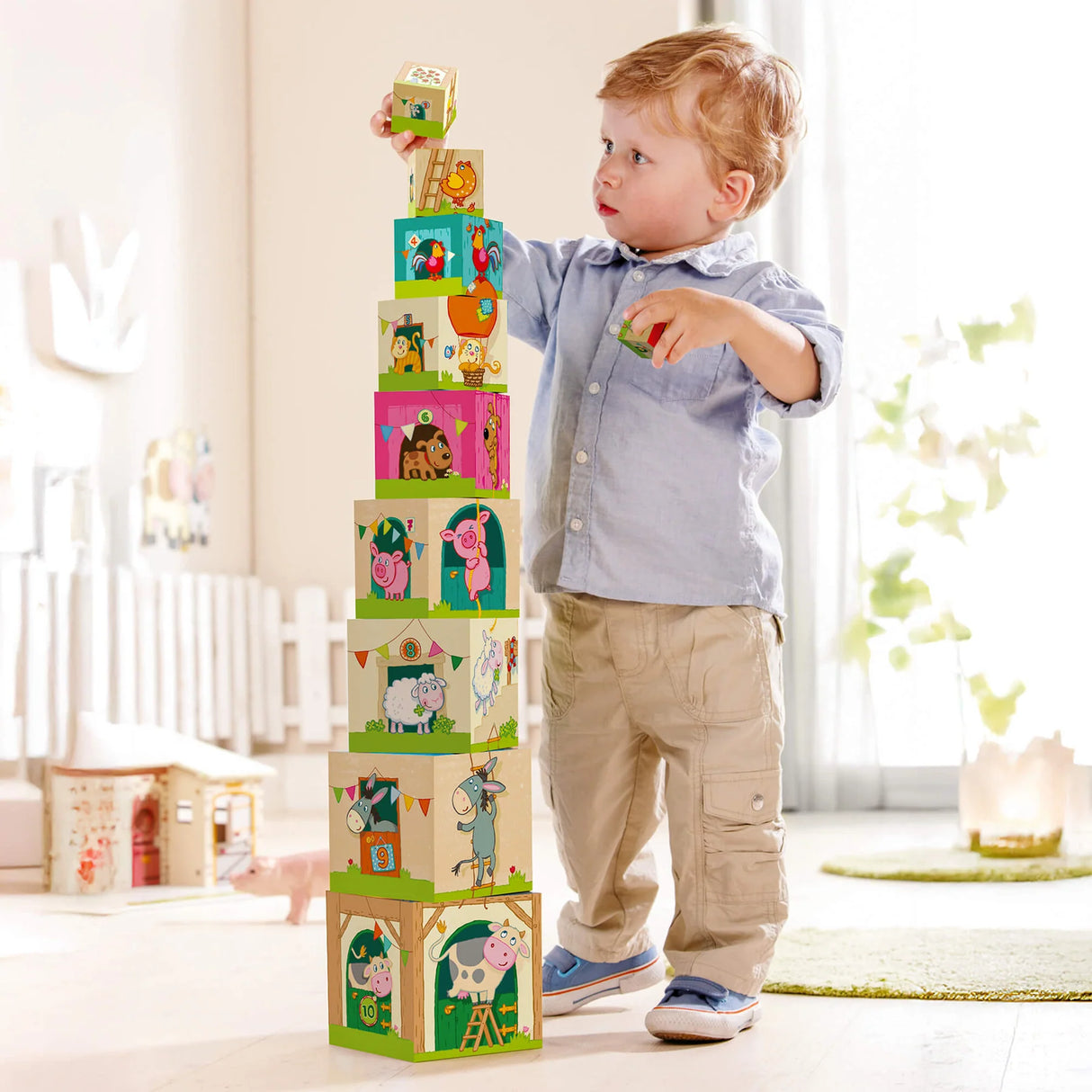 Toddler stacking colorful farm-themed cubes featuring animals and farm scenes in a bright, cozy playroom.