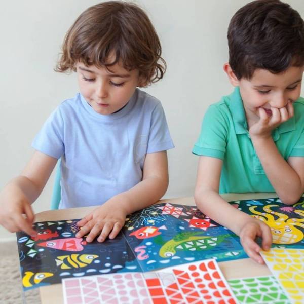 Two children creating a vibrant marine scene with the Poppik Sticker Panorama Aquarium stickers and colorful shapes