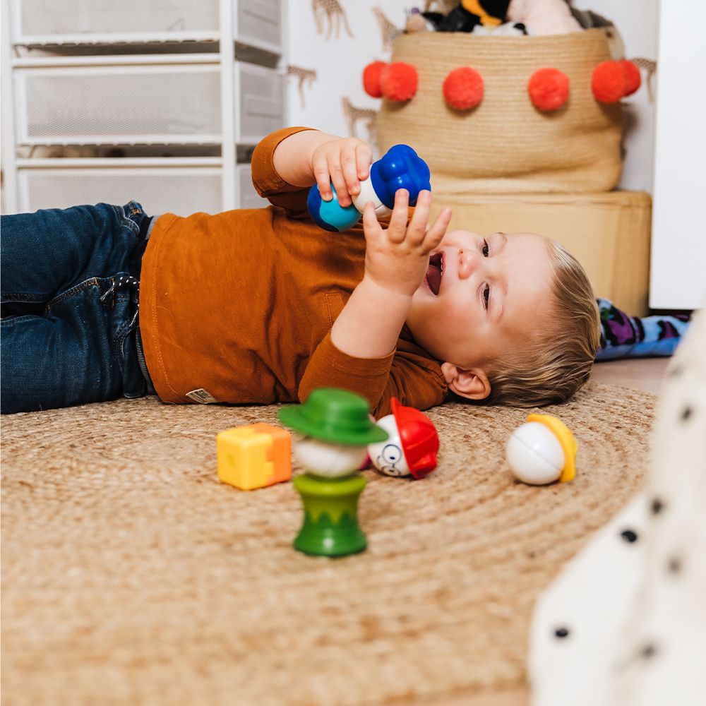 Child playing with colorful magnetic pieces of Smartmax My First People on a woven rug in a cozy room.