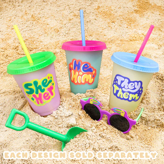 They/Them Pronouns Sticker on cup with pink lid and blue straw, shown on sand with other pronoun cups and beach toys.