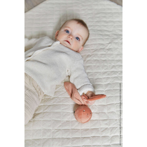 Baby lying on quilted blanket holding the soft 2.4 inch My Little Rattle Ball Bunny with large ears and bell inside