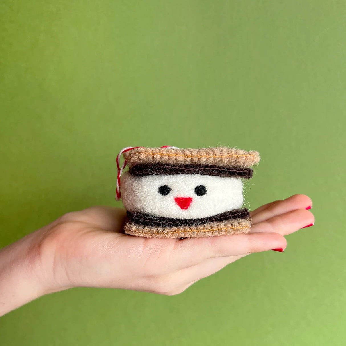 Smiling S'more Felt Ornament held in hand, showing felt graham crackers, chocolate, and a smiling marshmallow face.