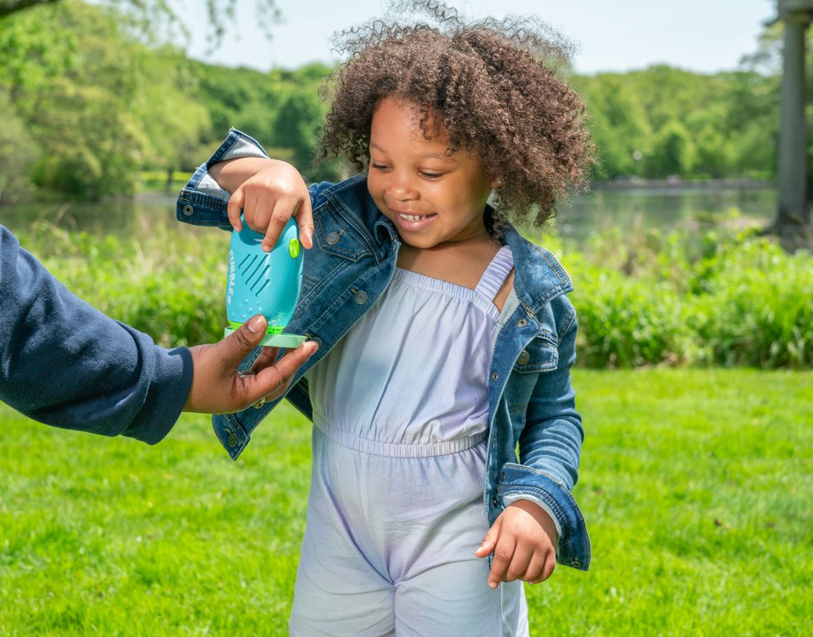 Child playing outdoors using Fubbles | Bubble Surge Mini Blaster with adult hand holding dip tray on green lawn.
