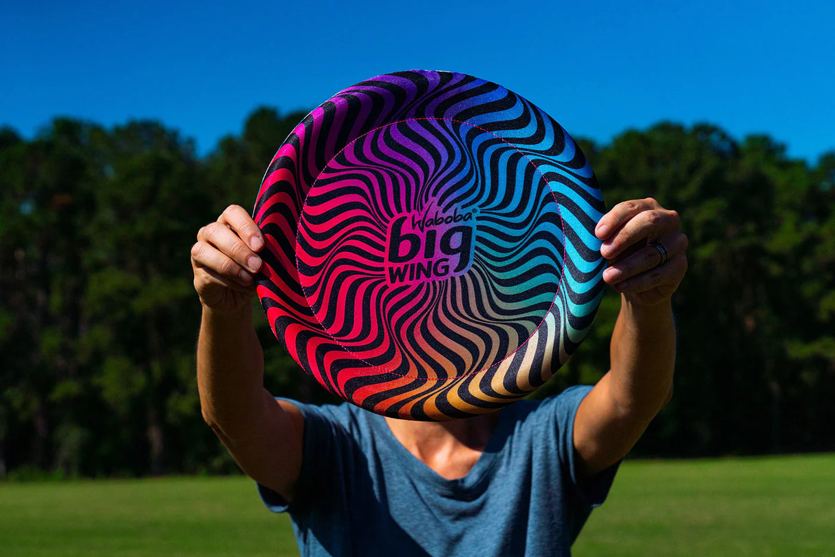Person holding colorful Waboba Big Wing fabric covered disc with vibrant swirl design outdoors on a sunny day