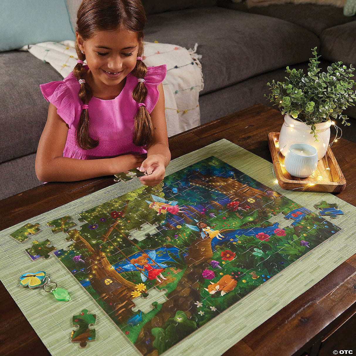 Young girl assembling PZ 100pc Seek&Find Fairies puzzle featuring a colorful forest scene with hidden glow-in-the-dark items.