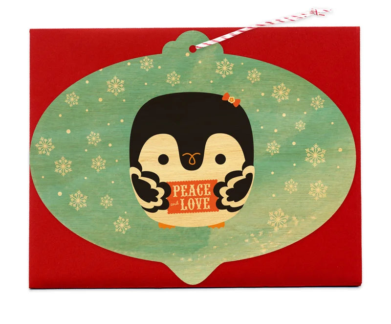 Penguin Ornament Wood Card featuring a cute penguin holding a Peace and Love sign on a snowy green background.