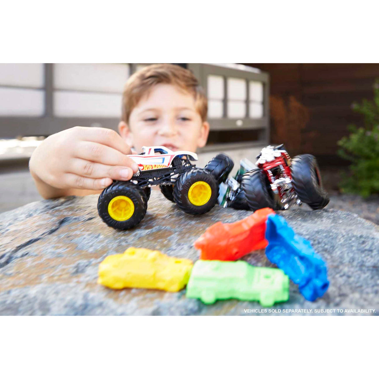 Child playing with Hot Wheels Monster Truck 1:64 scale die-cast vehicles crushing colorful cars outdoors.